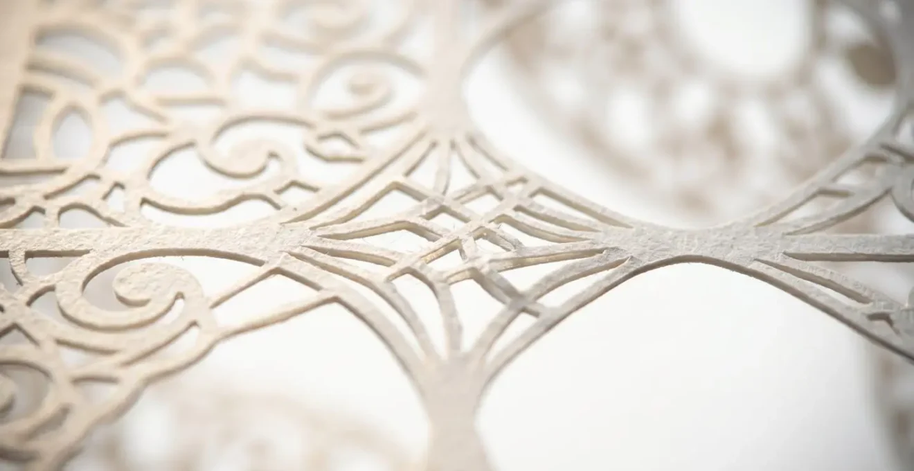 Détail macro d'un motif en dentelle de papier montrant les ponts de matière invisibles qui maintiennent la structure